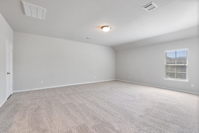 carpeted empty room featuring visible vents, a textured ceiling, lofted ceiling, and baseboards