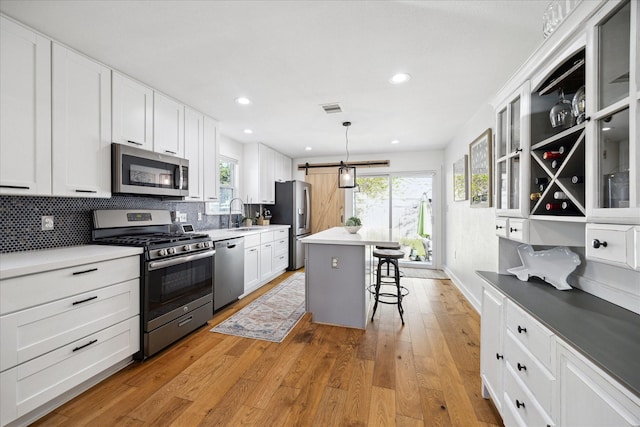 kitchen featuring visible vents, stainless steel appliances, light wood-style floors, a kitchen breakfast bar, and backsplash