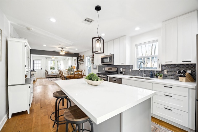 kitchen with light wood-type flooring, decorative backsplash, appliances with stainless steel finishes, a ceiling fan, and a sink