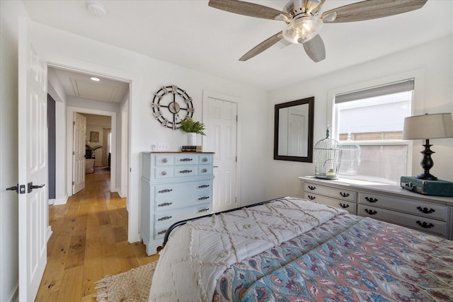 bedroom featuring baseboards, attic access, light wood-type flooring, and ceiling fan