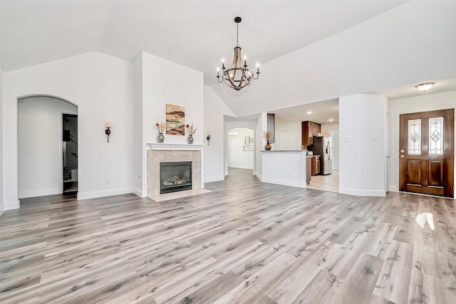 unfurnished living room with arched walkways, a notable chandelier, baseboards, and light wood-style floors