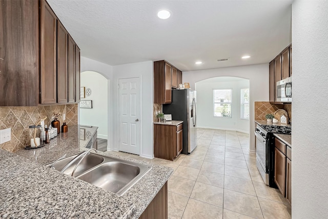 kitchen featuring visible vents, a sink, arched walkways, appliances with stainless steel finishes, and light tile patterned floors