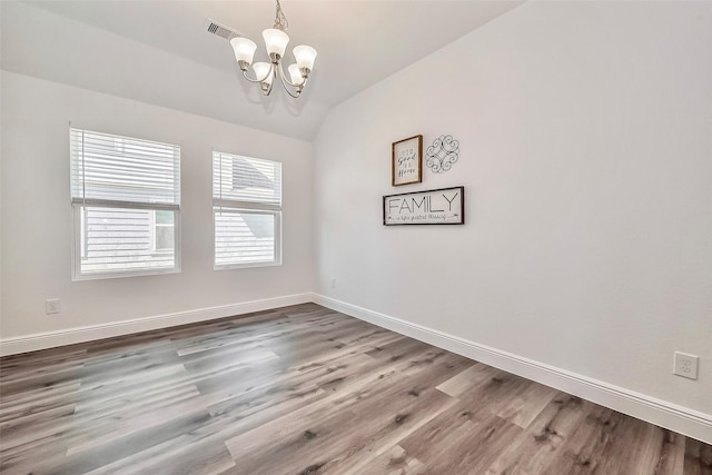 spare room with baseboards, a notable chandelier, lofted ceiling, and wood finished floors