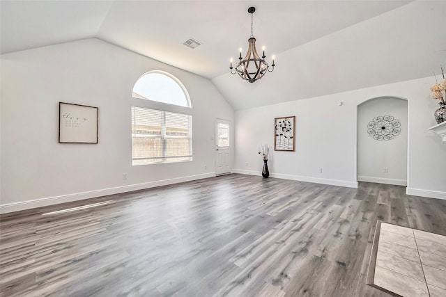 unfurnished living room with wood finished floors, visible vents, baseboards, an inviting chandelier, and lofted ceiling