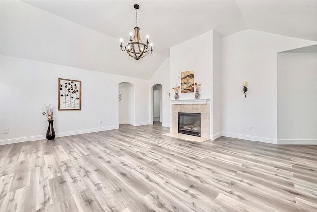 unfurnished living room featuring baseboards, light wood-type flooring, lofted ceiling, an inviting chandelier, and arched walkways