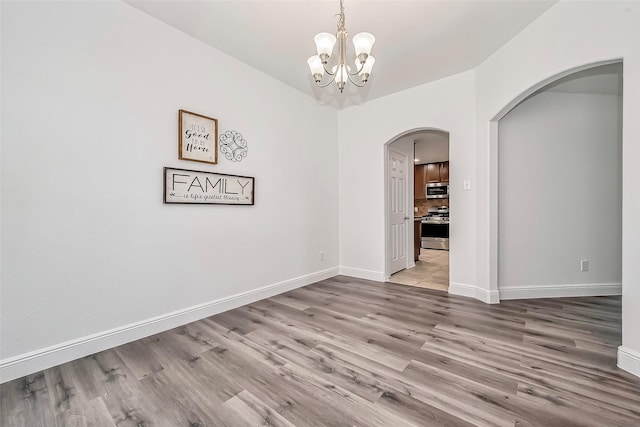 empty room with arched walkways, baseboards, an inviting chandelier, and wood finished floors