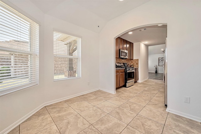 kitchen with light tile patterned floors, arched walkways, stainless steel appliances, decorative backsplash, and vaulted ceiling