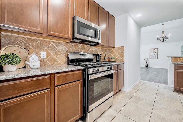 kitchen featuring tasteful backsplash, stainless steel appliances, light tile patterned floors, baseboards, and a chandelier