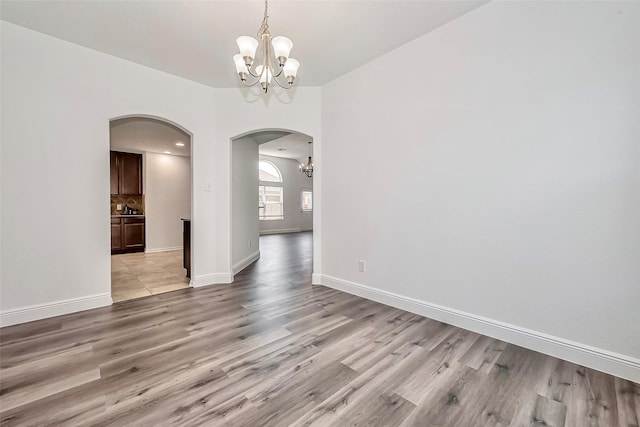 unfurnished room featuring a notable chandelier, baseboards, arched walkways, and light wood finished floors