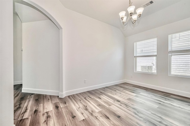 unfurnished room with arched walkways, visible vents, a notable chandelier, and wood finished floors