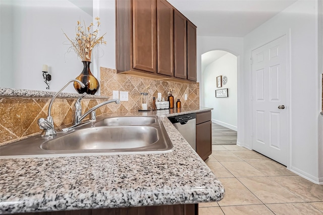 kitchen featuring a sink, backsplash, arched walkways, light tile patterned floors, and dishwasher