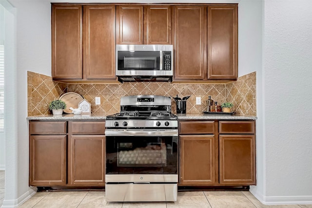 kitchen with light stone counters, stainless steel appliances, tasteful backsplash, and light tile patterned flooring