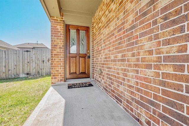 doorway to property featuring brick siding and fence