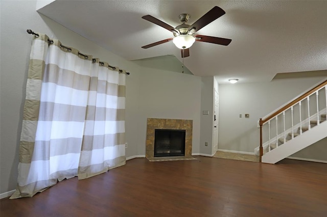 unfurnished living room with baseboards, ceiling fan, stairs, a fireplace, and wood finished floors