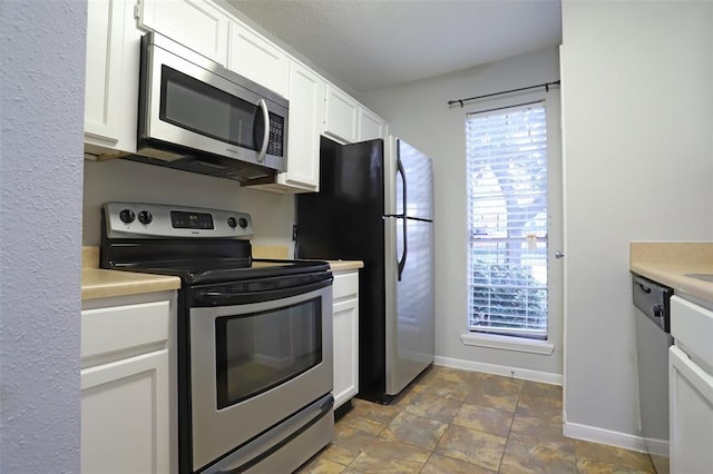 kitchen with baseboards, light countertops, white cabinets, stone finish floor, and appliances with stainless steel finishes