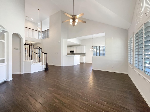 unfurnished living room featuring baseboards, arched walkways, dark wood-style floors, and ceiling fan with notable chandelier