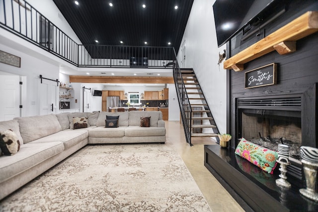 living area featuring a fireplace with raised hearth, concrete floors, stairs, recessed lighting, and a towering ceiling