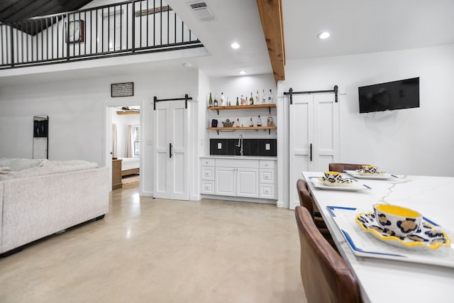 kitchen with finished concrete floors, a barn door, beam ceiling, recessed lighting, and white cabinetry