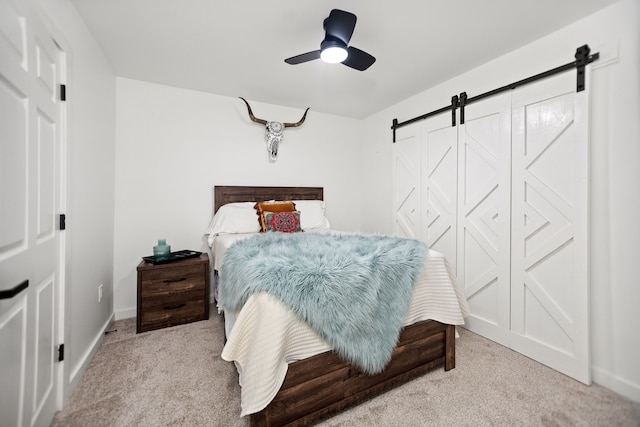 bedroom featuring ceiling fan, baseboards, a barn door, and carpet floors