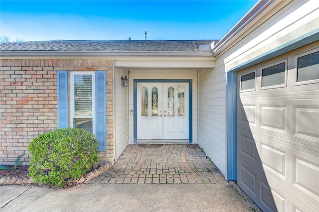 property entrance featuring brick siding, french doors, a shingled roof, and a garage