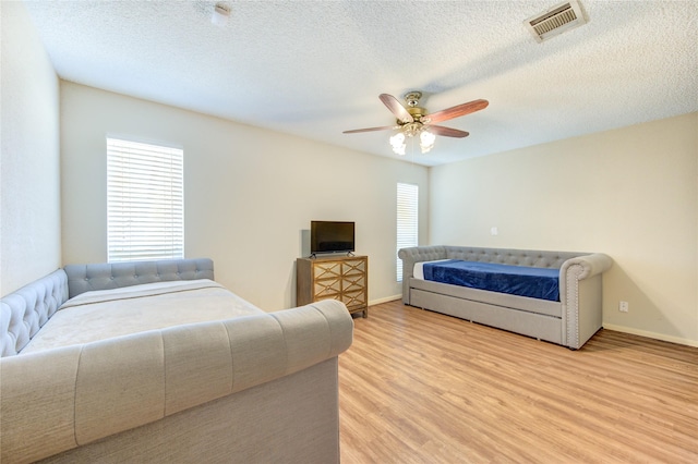 bedroom featuring visible vents, baseboards, light wood-style flooring, a textured ceiling, and a ceiling fan