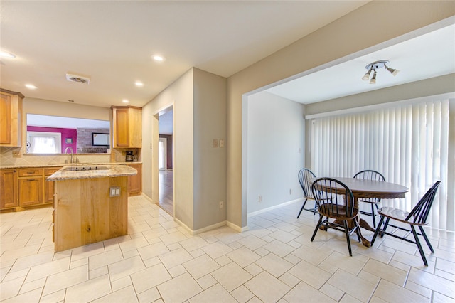 kitchen featuring visible vents, baseboards, a kitchen island, a sink, and decorative backsplash