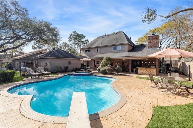 view of swimming pool with fence, a diving board, a pool with connected hot tub, a patio area, and outdoor dry bar