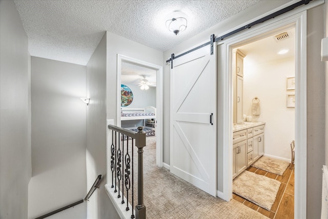 hall featuring visible vents, wood tiled floor, a barn door, an upstairs landing, and a textured ceiling