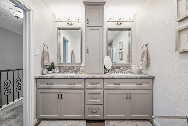 bathroom with a sink, double vanity, and a textured wall