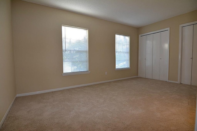 unfurnished bedroom with baseboards, multiple closets, and carpet floors