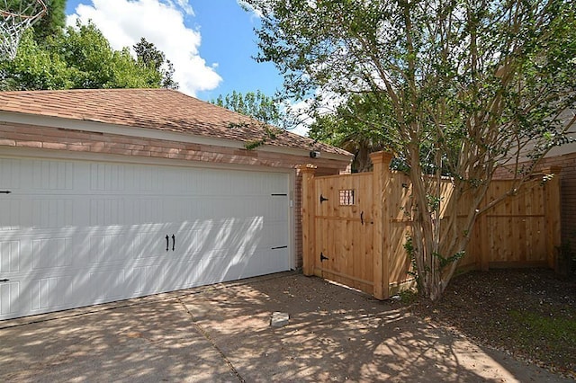 garage with a gate, concrete driveway, and fence