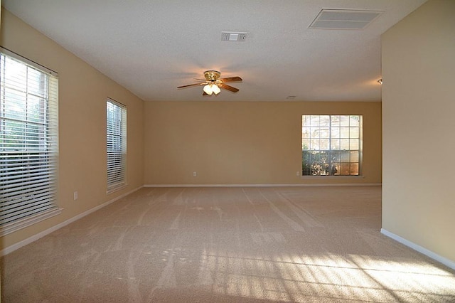 empty room featuring a wealth of natural light, visible vents, and a ceiling fan