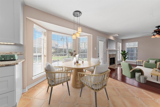 dining room featuring light tile patterned flooring, a fireplace, baseboards, and ceiling fan