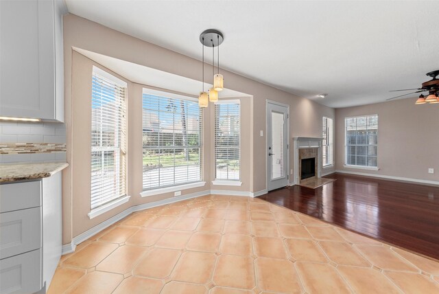 unfurnished living room with a high end fireplace, baseboards, light wood-style flooring, and a ceiling fan