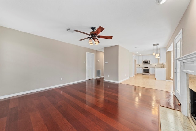 unfurnished living room featuring a ceiling fan, visible vents, a high end fireplace, and light wood-type flooring