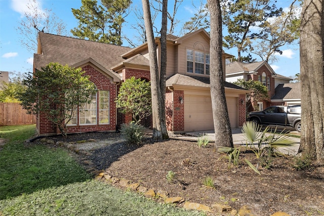 traditional-style house featuring driveway, fence, roof with shingles, an attached garage, and brick siding