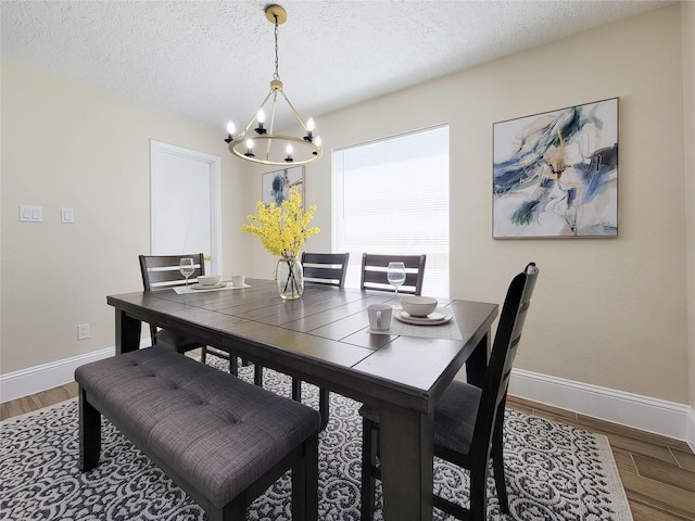 dining space featuring a notable chandelier, a textured ceiling, baseboards, and wood finished floors