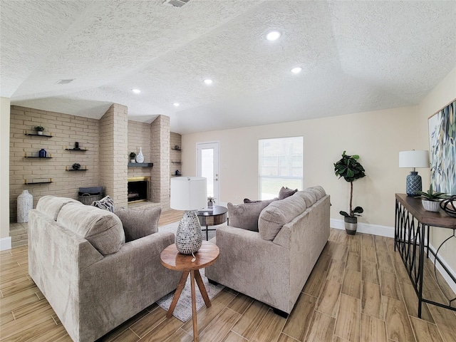 living area with baseboards, wood finish floors, lofted ceiling, a textured ceiling, and a brick fireplace