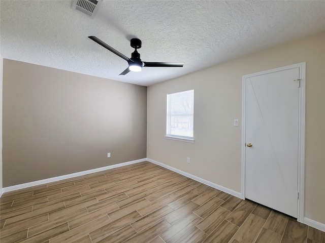 unfurnished room with visible vents, wood finish floors, baseboards, ceiling fan, and a textured ceiling