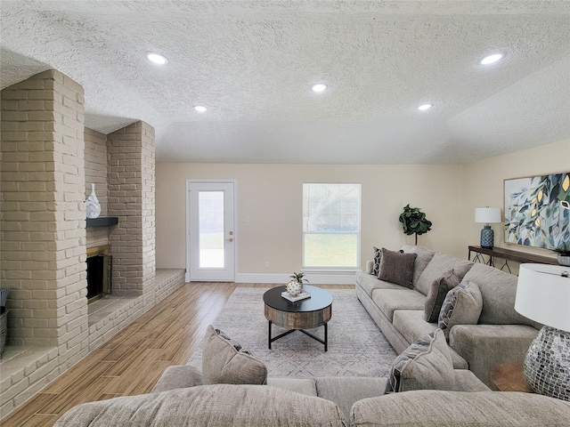 living area featuring a brick fireplace, wood finished floors, baseboards, and a textured ceiling