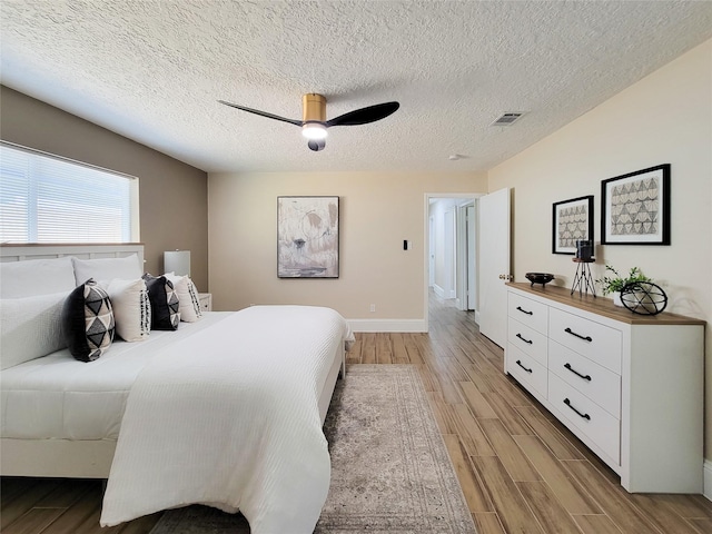 bedroom featuring visible vents, baseboards, ceiling fan, light wood-style flooring, and a textured ceiling