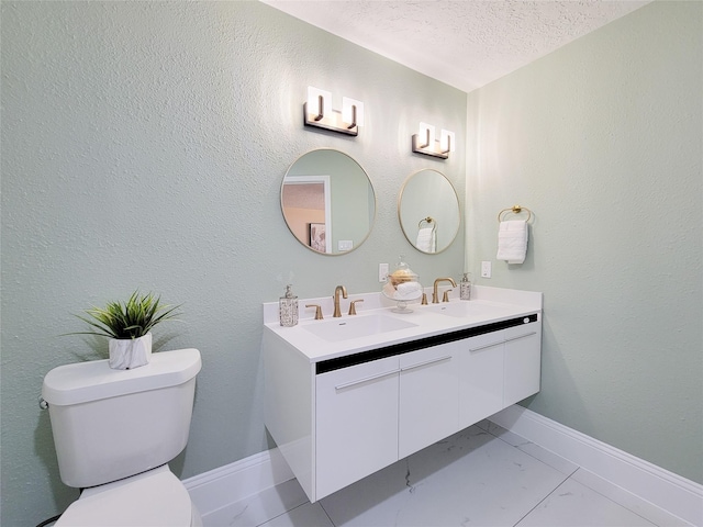 bathroom with a textured ceiling, double vanity, toilet, and a sink