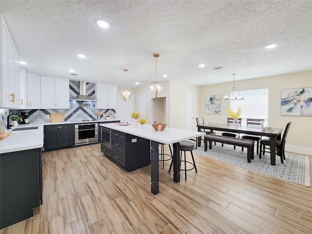 kitchen with dark cabinetry, a sink, light countertops, appliances with stainless steel finishes, and wall chimney range hood