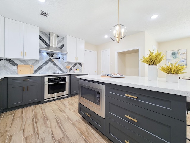 kitchen with visible vents, decorative backsplash, appliances with stainless steel finishes, white cabinets, and wall chimney exhaust hood