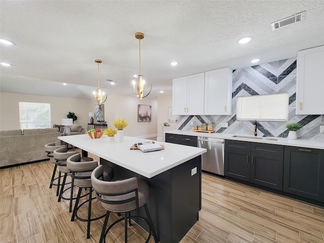 kitchen featuring visible vents, a sink, stainless steel dishwasher, white cabinetry, and light countertops