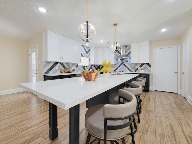 kitchen with decorative backsplash, white cabinets, a breakfast bar, and wall chimney range hood