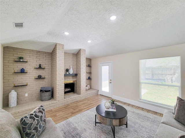 living area with light wood finished floors, visible vents, vaulted ceiling, a fireplace, and a textured ceiling