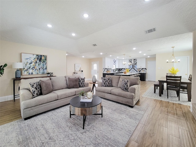 living area with visible vents, a chandelier, recessed lighting, light wood-style floors, and a textured ceiling