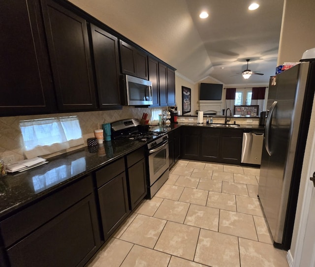 kitchen featuring ceiling fan, lofted ceiling, dark stone countertops, appliances with stainless steel finishes, and a sink