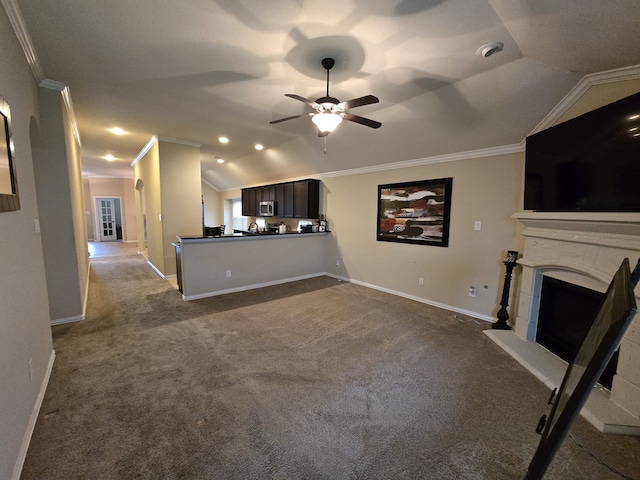 unfurnished living room featuring lofted ceiling, a fireplace with raised hearth, ceiling fan, crown molding, and dark carpet